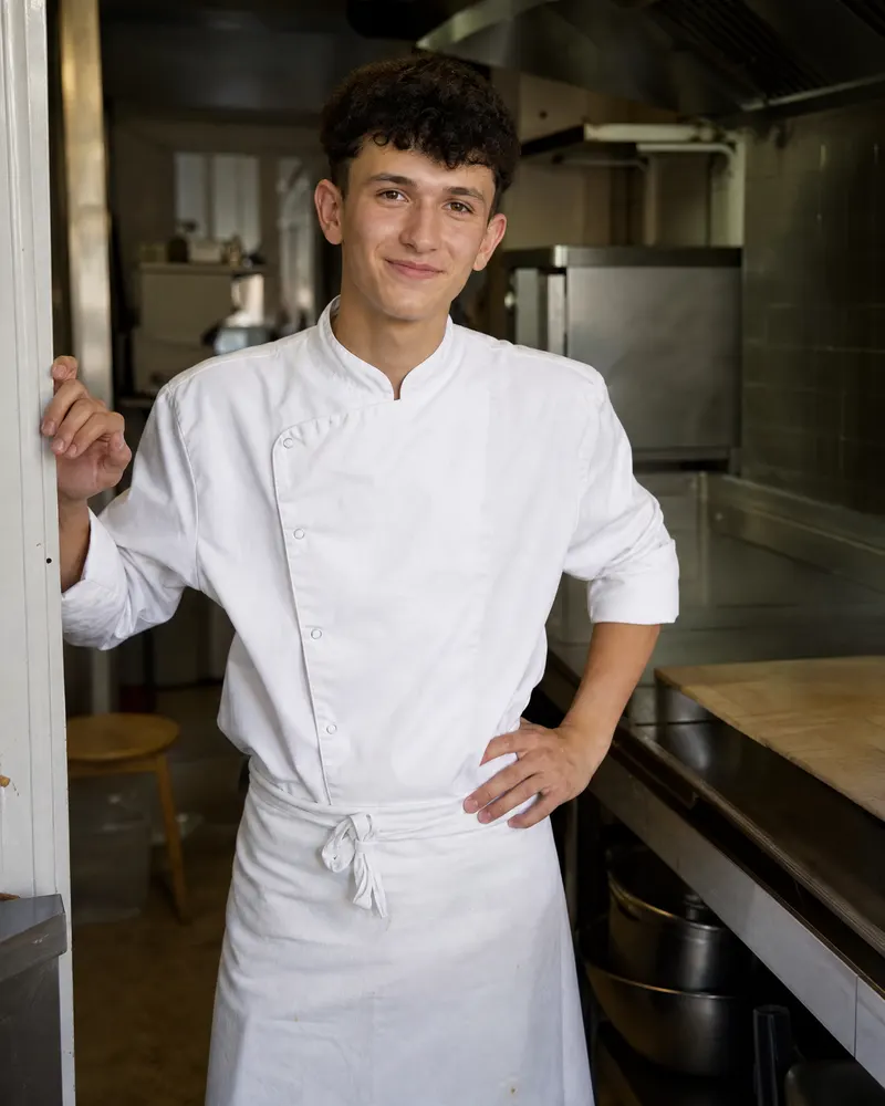 Théo, 19 ans, en tenue de cuisine, dans la cuisine du restaurant.
